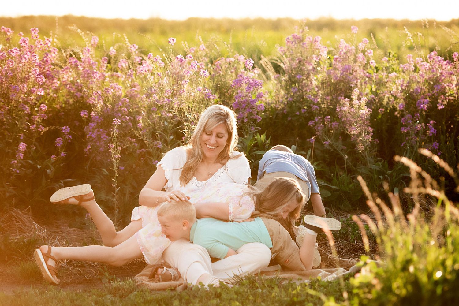 Playful couple lying in a wildflower meadow during golden hour surrounded by blooming flowers.