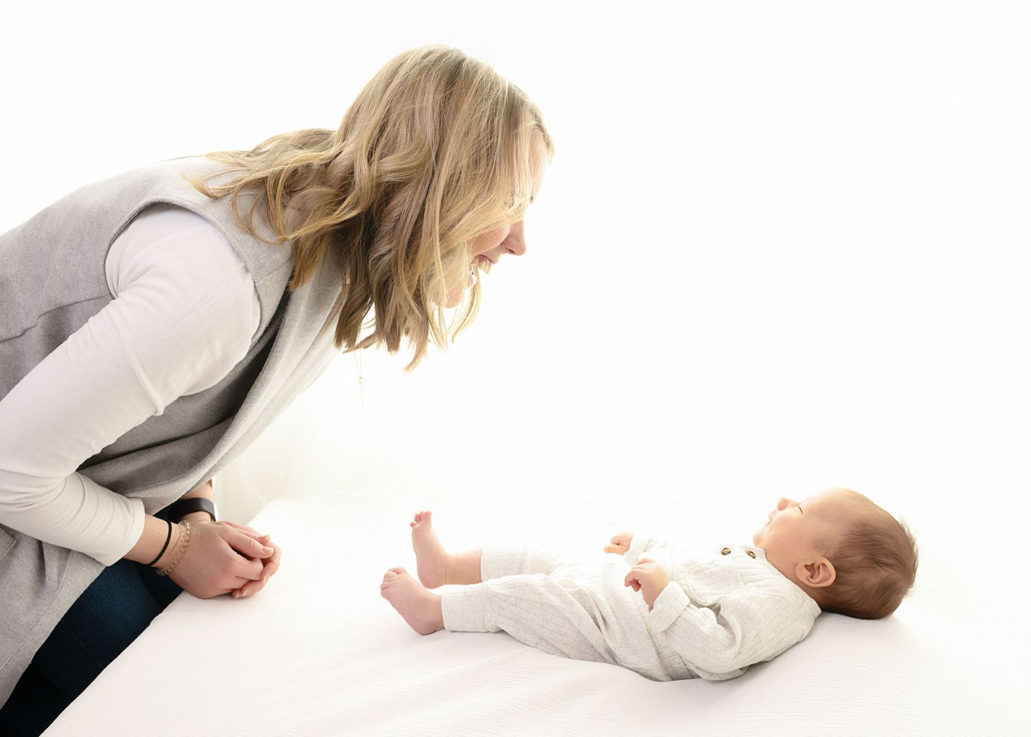 Parent leaning over to interact with baby lying on white background during photo session.