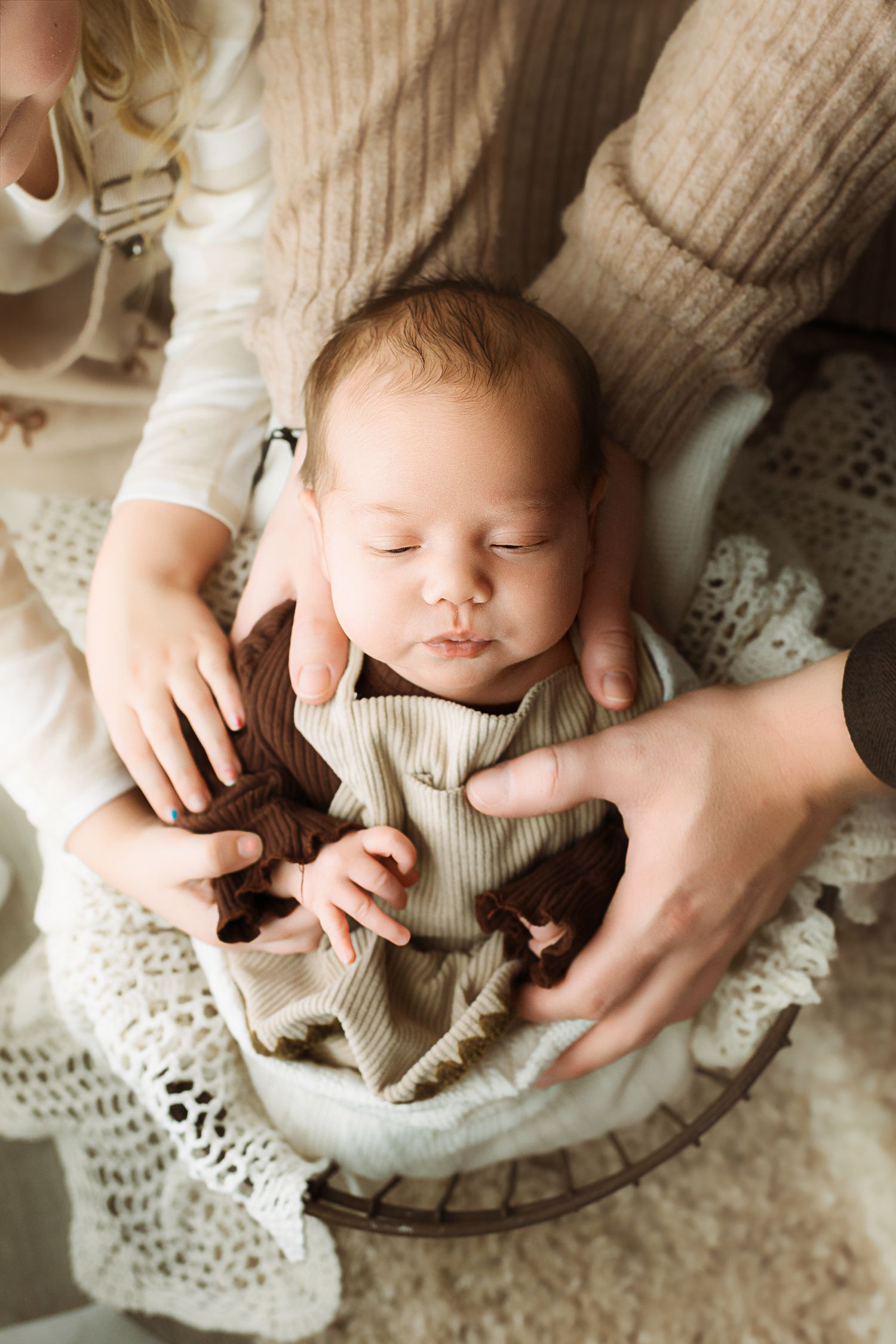 A sleeping baby in cream knit clothing lies on a round lace doily with gentle hands providing comfort.
