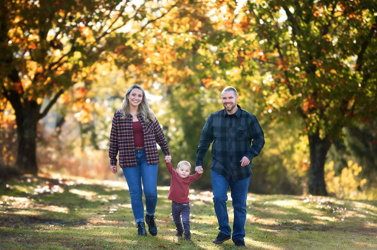 Family strolling through a park with golden fall foliage and sunlight filtering through the trees.