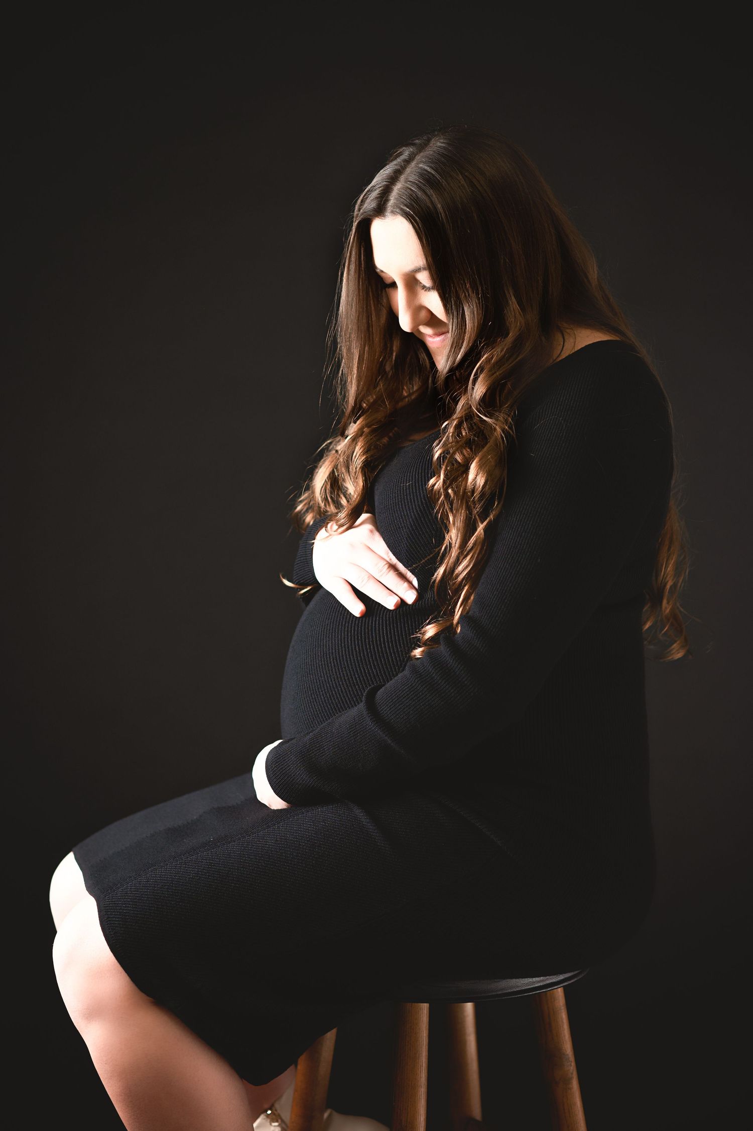 Artistic maternity silhouette series against dark background showing pregnant woman in black dress.