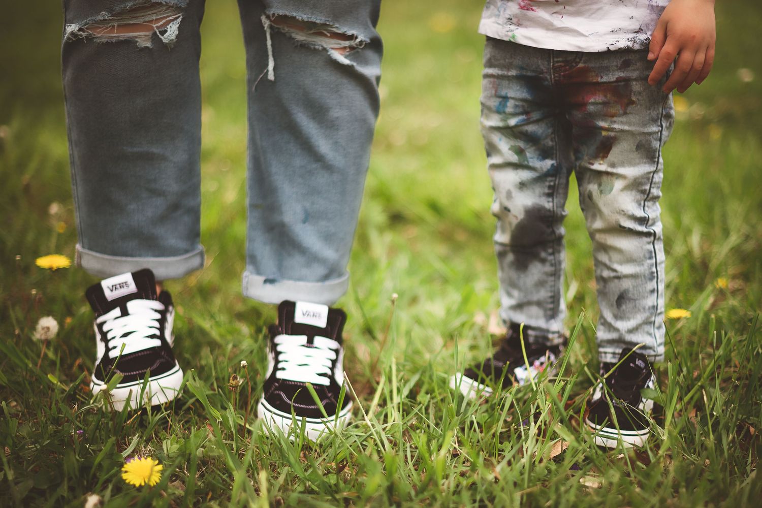 Close-up of children's feet wearing sneakers standing in grass with yellow flowers.