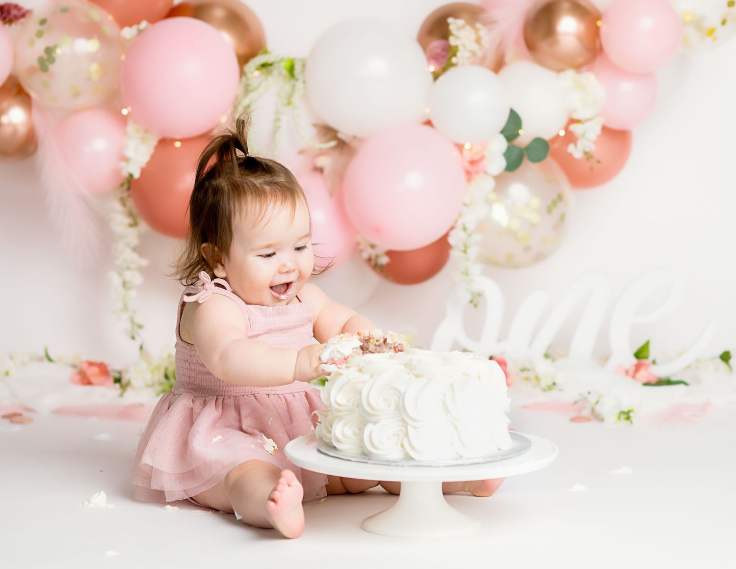 Pink and white balloon arch with floral accents and birthday cake setup.