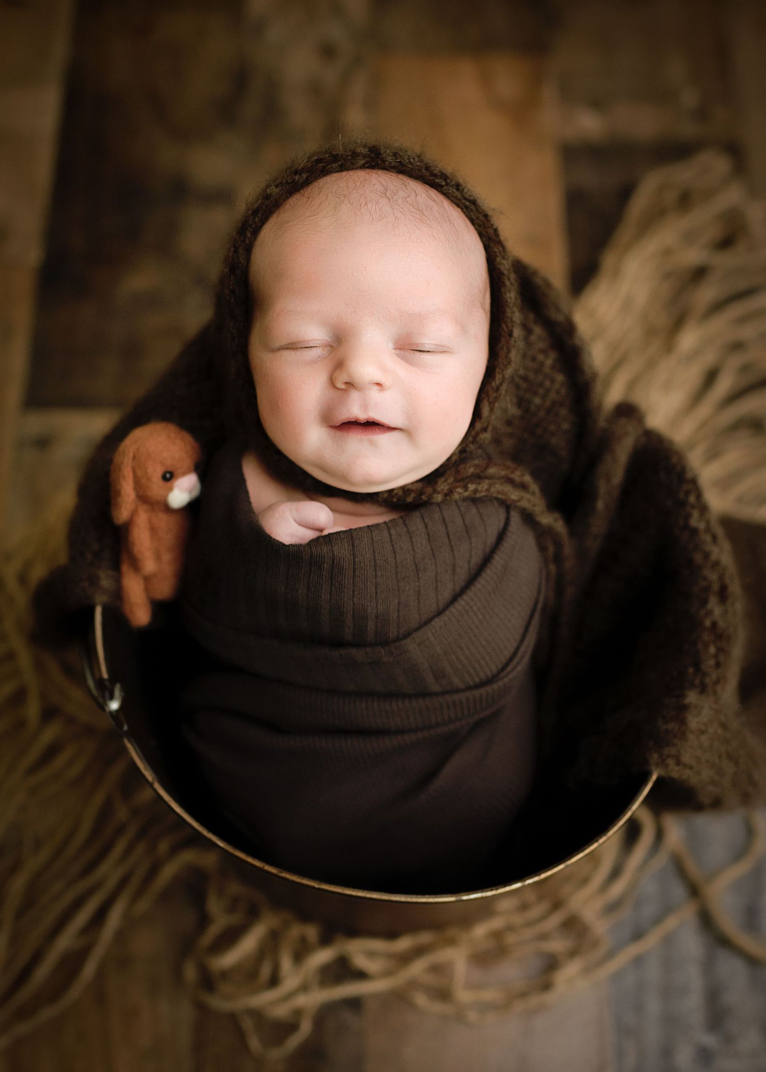 Close-up series of sleeping newborn in brown wrap nestled in round bowl.