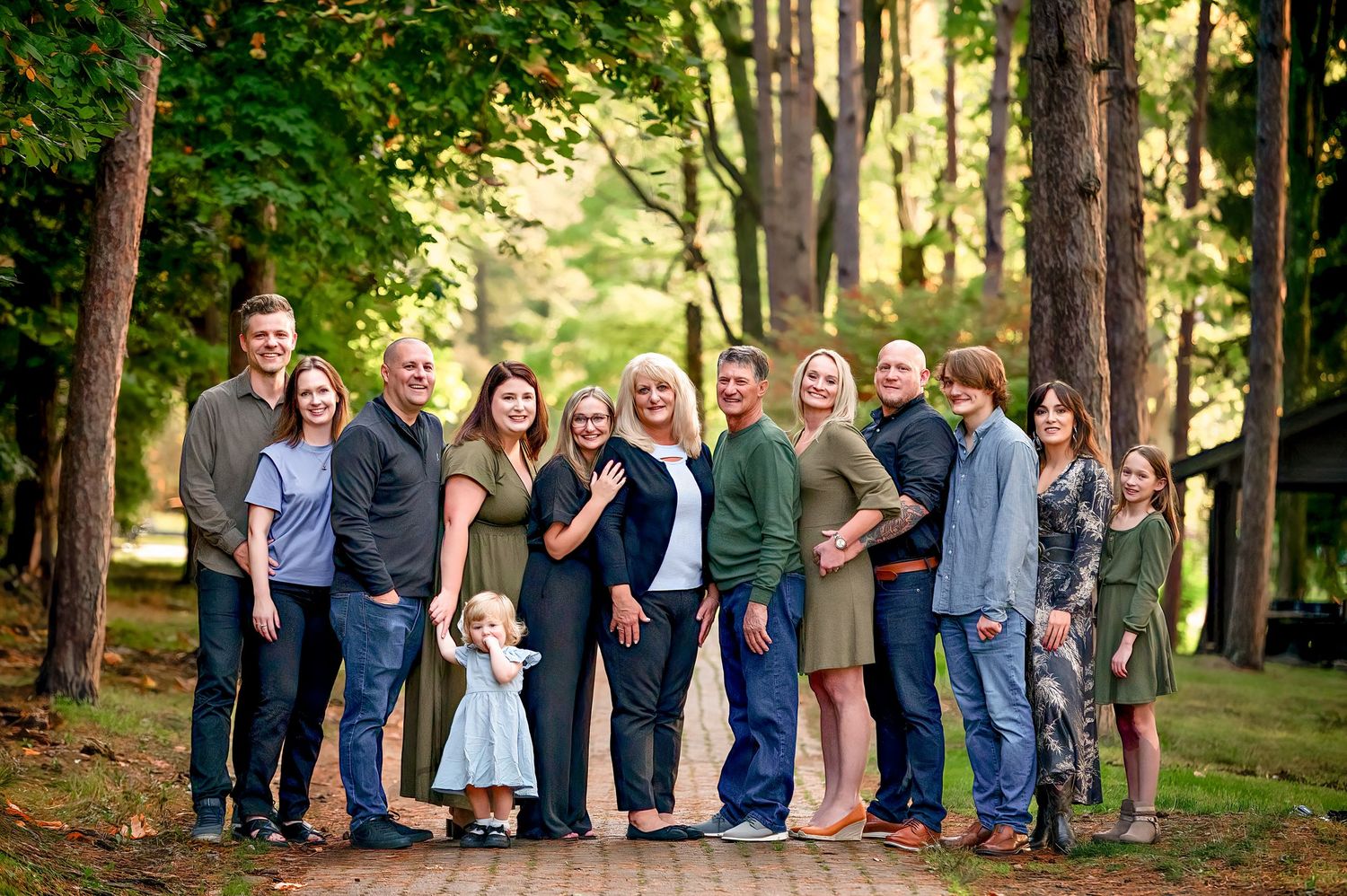 Large extended family group poses together in a wooded outdoor setting during summer.