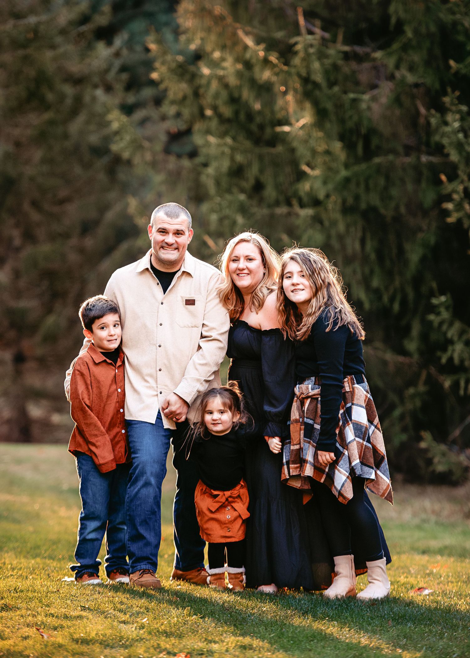 Family portrait session on grassy hill during golden hour with casual coordinated outfits.