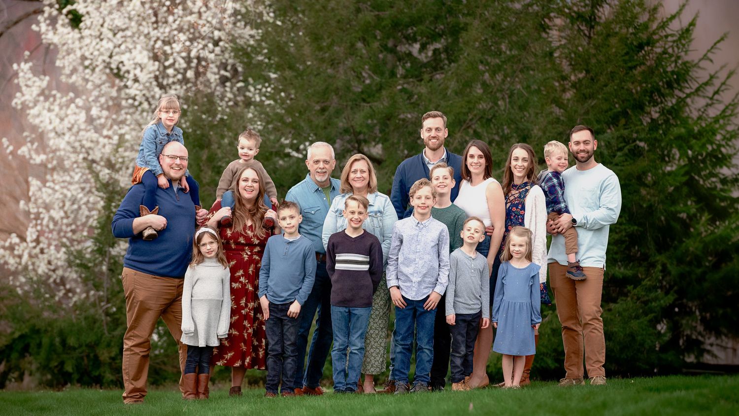 Extended family group poses together outdoors with blooming cherry trees in the background.