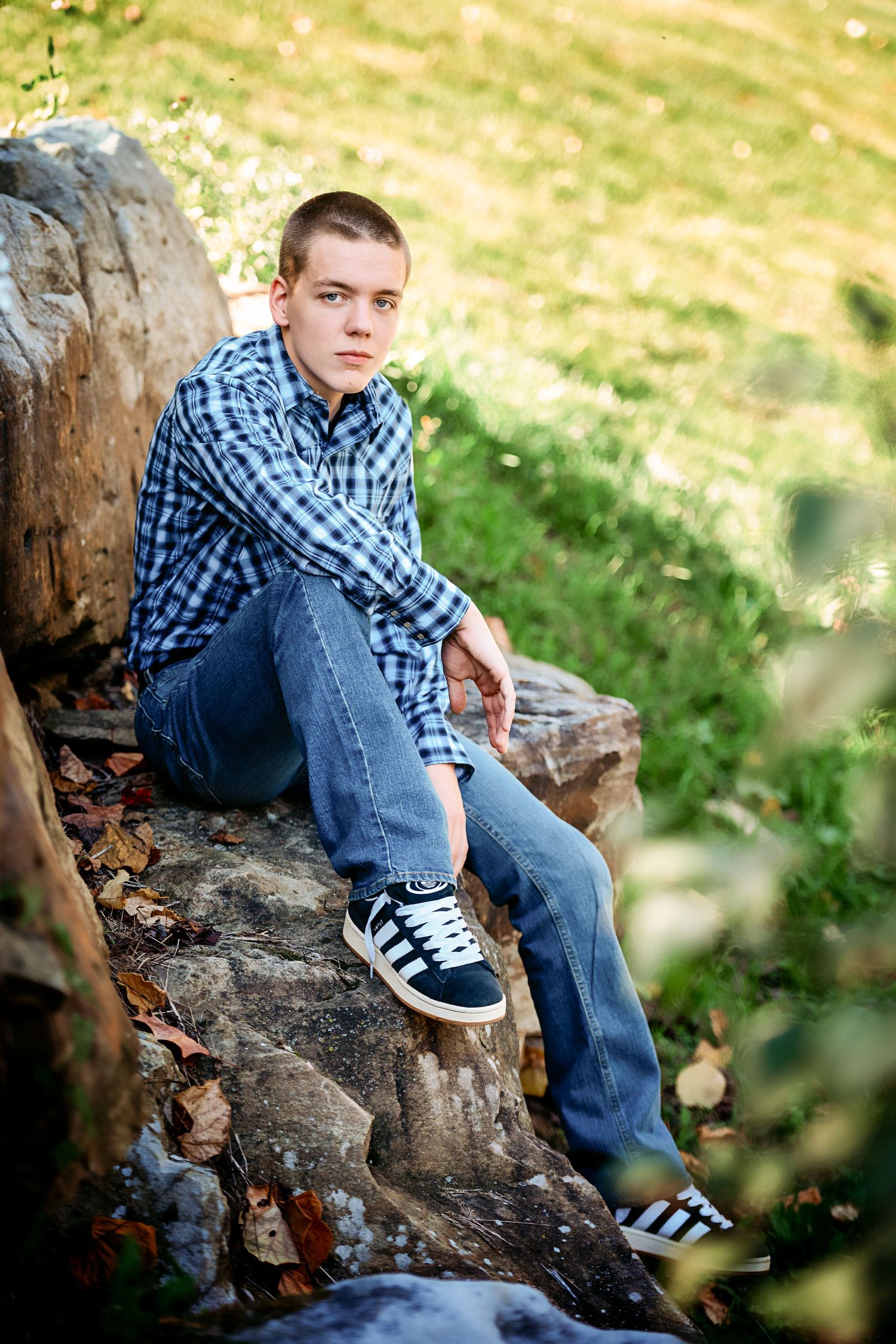 Outdoor portrait on rocky terrain featuring plaid shirt and sneakers against natural background.
