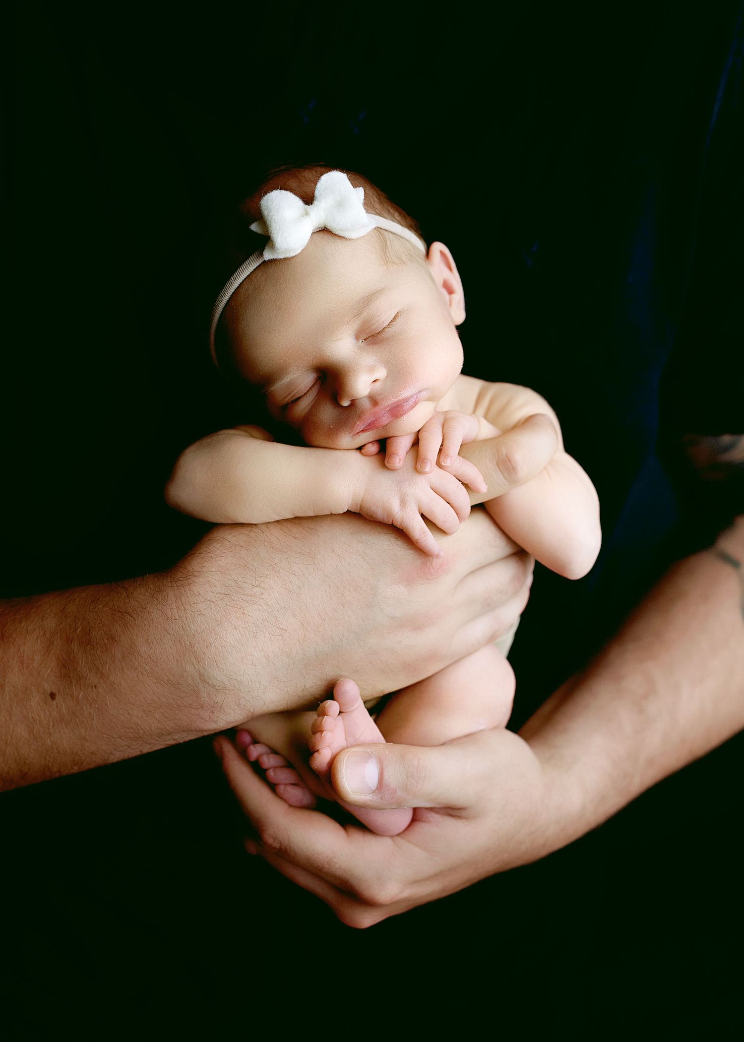 Series of intimate newborn portraits showing baby cradled in adult hands against dark backdrop.