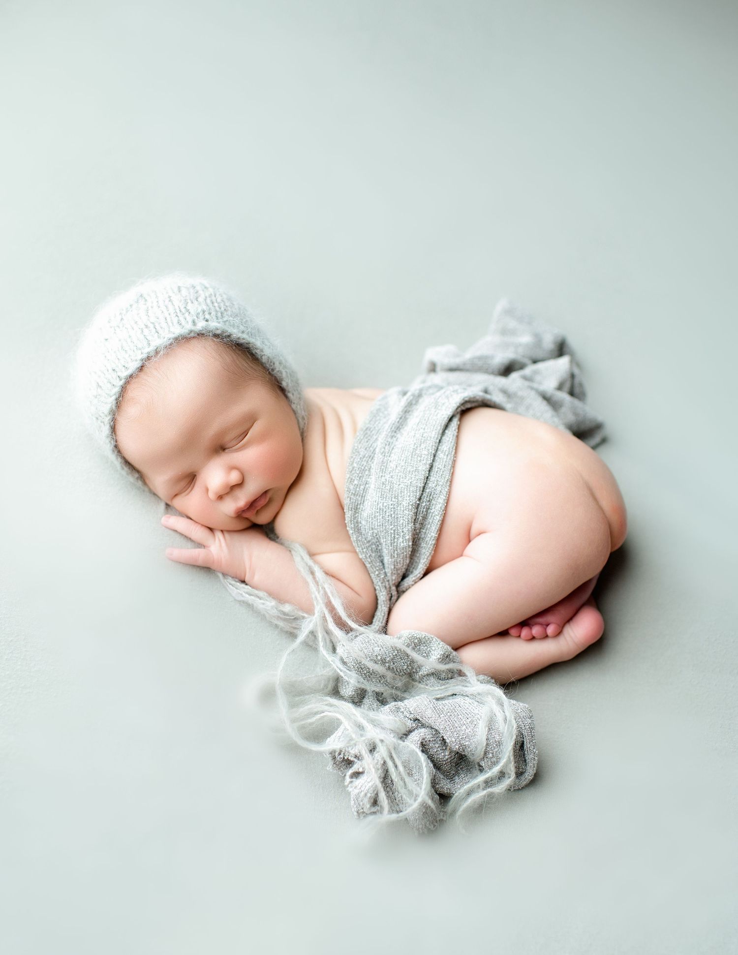 Sleeping newborn in grey wrap posed on mint green backdrop with fabric details.
