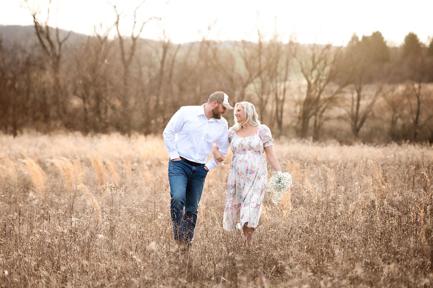 Couple walking together through a golden field at sunset in casual attire.