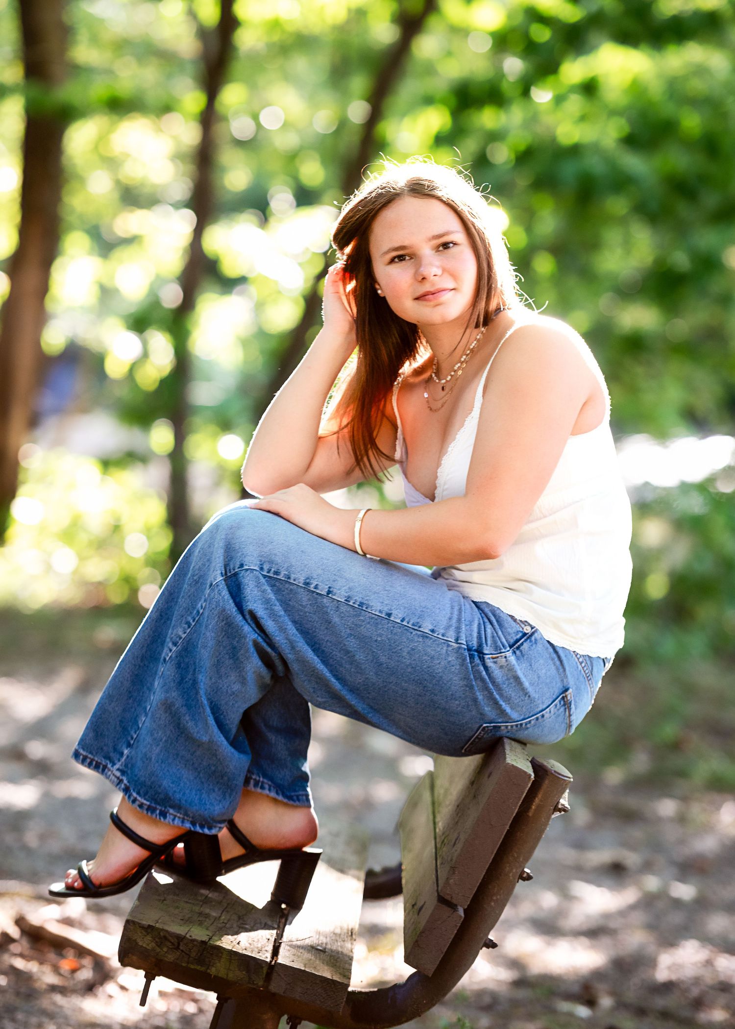Rustic outdoor poses on wooden bench wearing white top and jeans in natural setting.