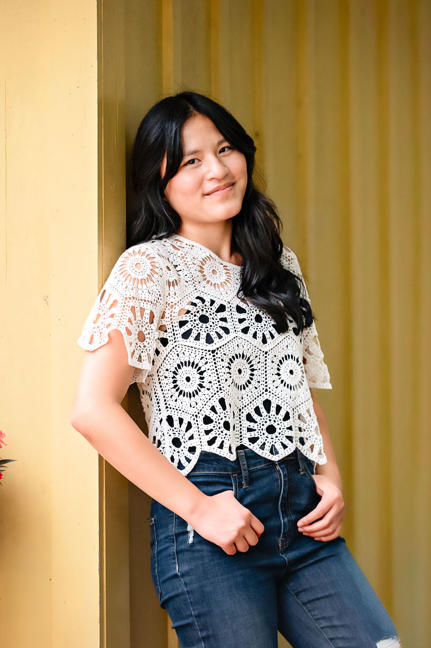 Fashion series against yellow wall showing details of white crochet top and dark denim jeans.