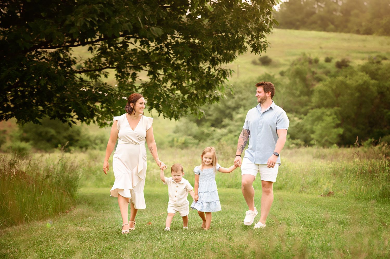 A family walks together through a sunlit meadow on a warm summer evening.