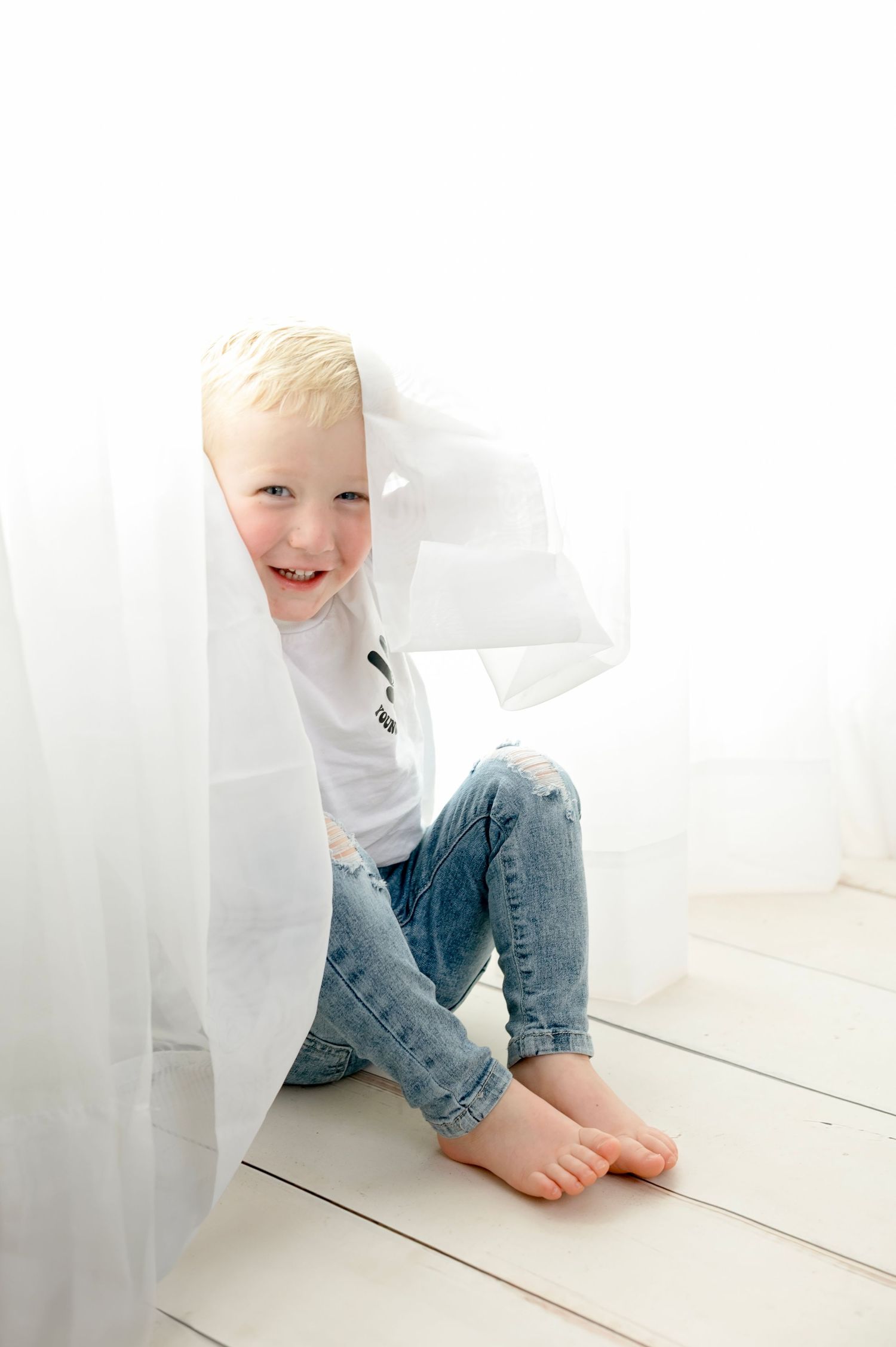 White curtain backdrop with child playing on wooden floor.