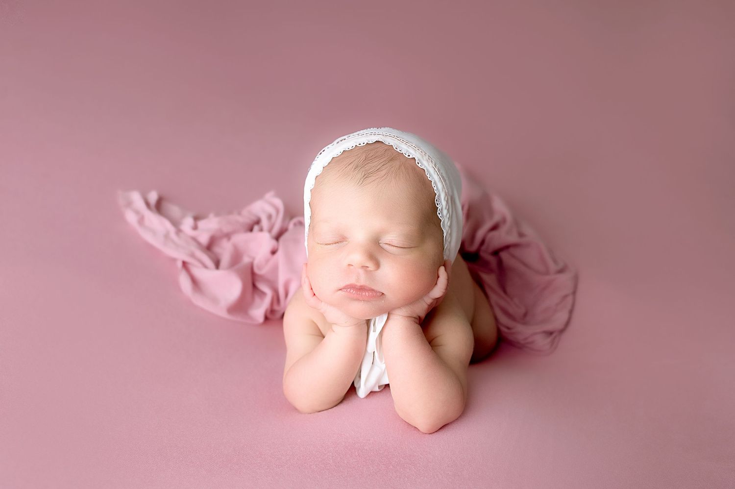 Artistic newborn photography series with baby on pink backdrop in gentle poses.