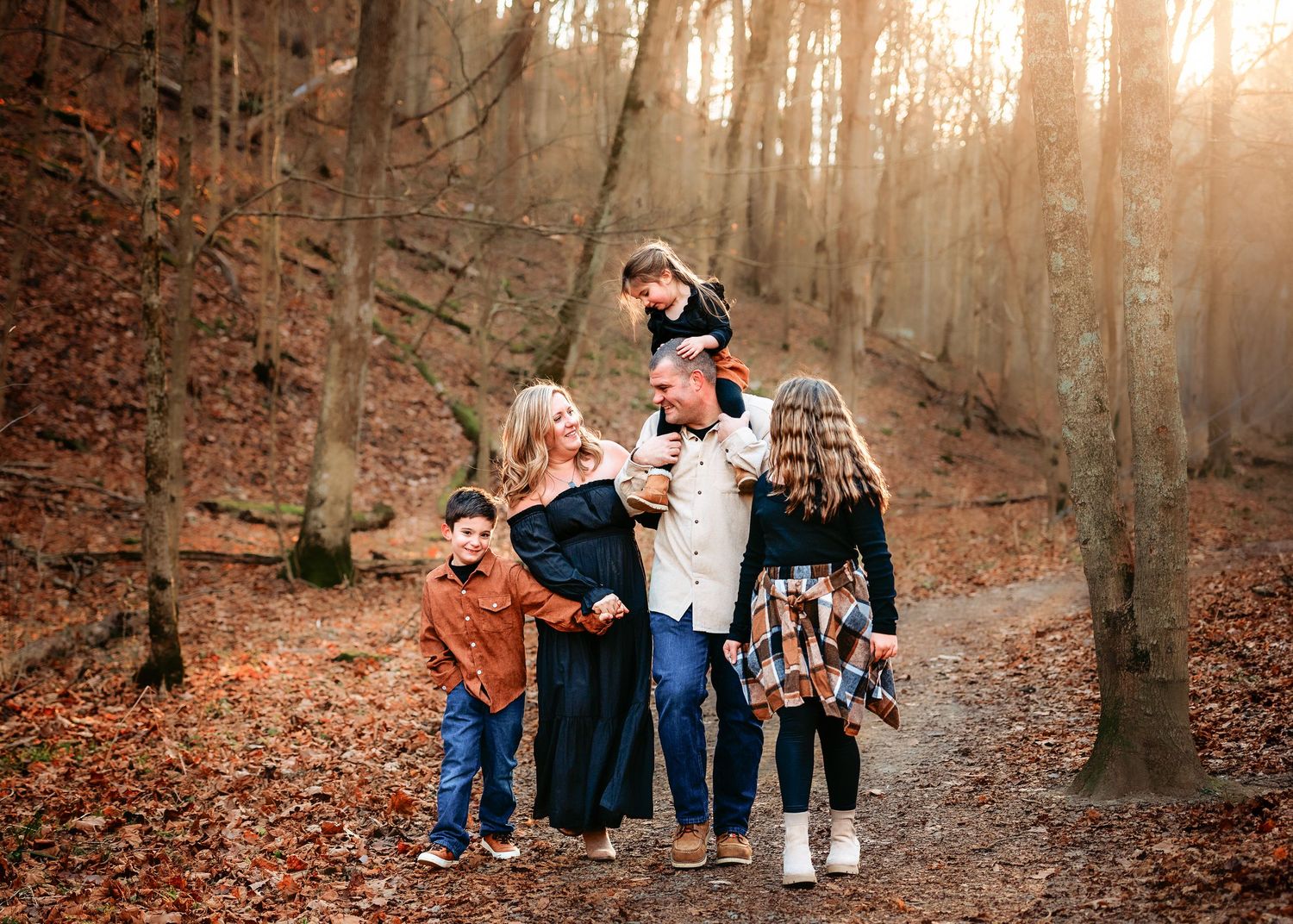 Family walking together on autumn forest path during golden hour.