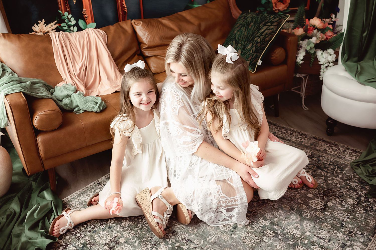 Family wearing cream colored dresses sitting together on brown leather couch.