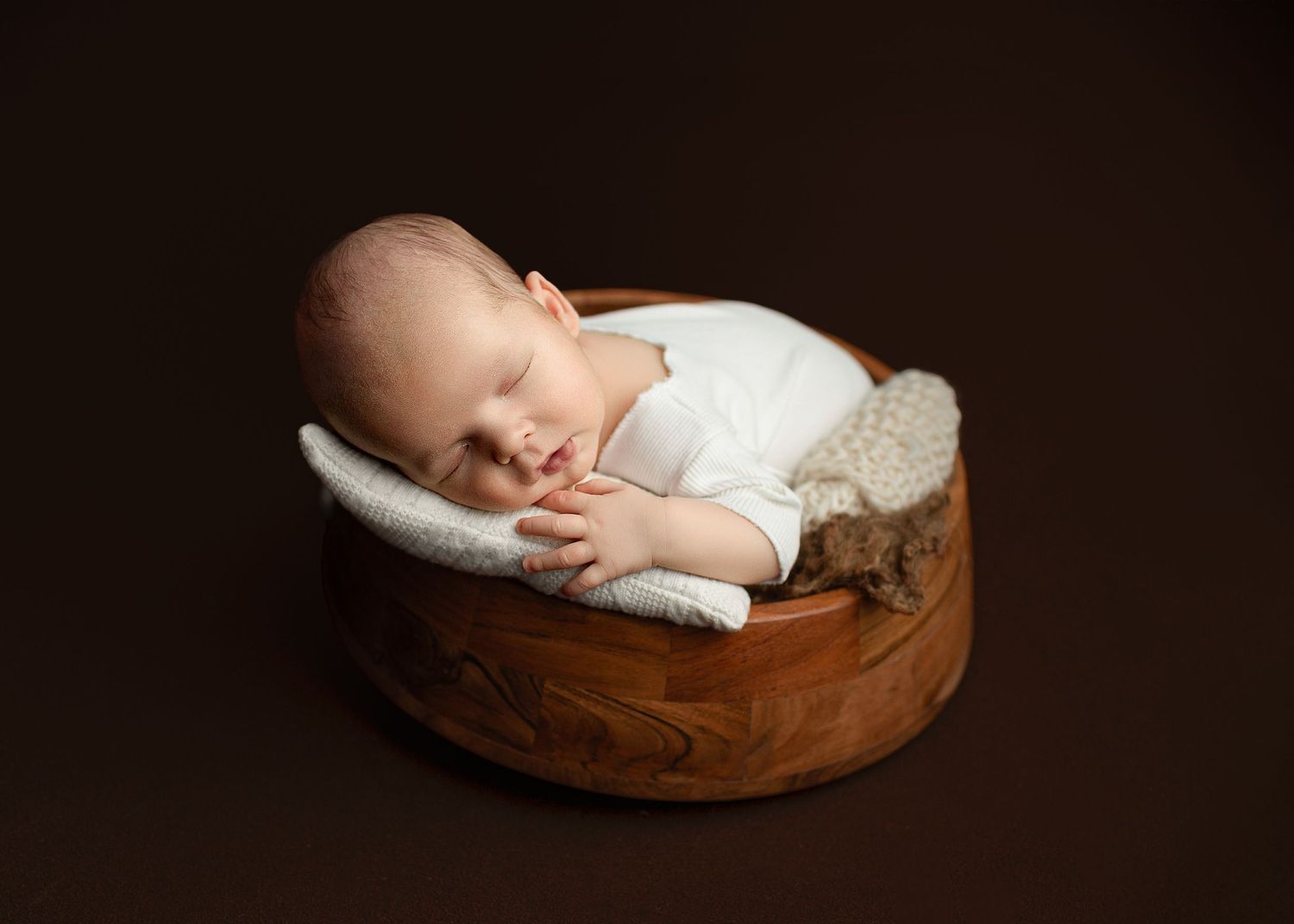 Peaceful sleeping newborn baby resting in wooden bowl with dark dramatic lighting.