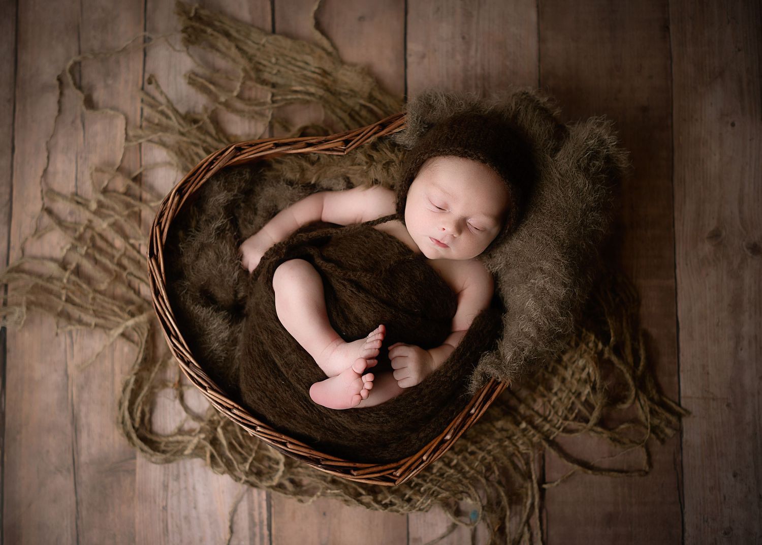 Artistic newborn photography with baby lying on textured brown backdrop.