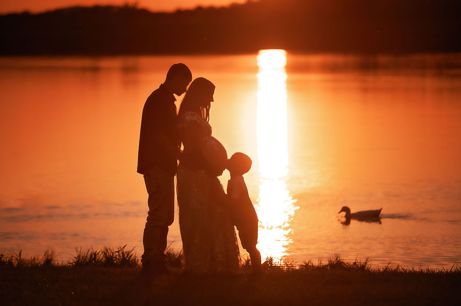 Silhouetted figures share a romantic moment against a vibrant orange sunset over water.