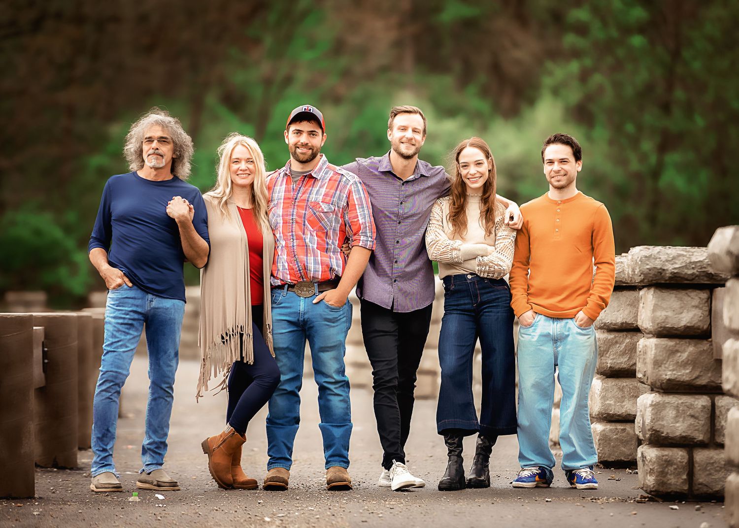 A group of six people stand together on a stone bridge wearing casual fall attire in an outdoor setting.