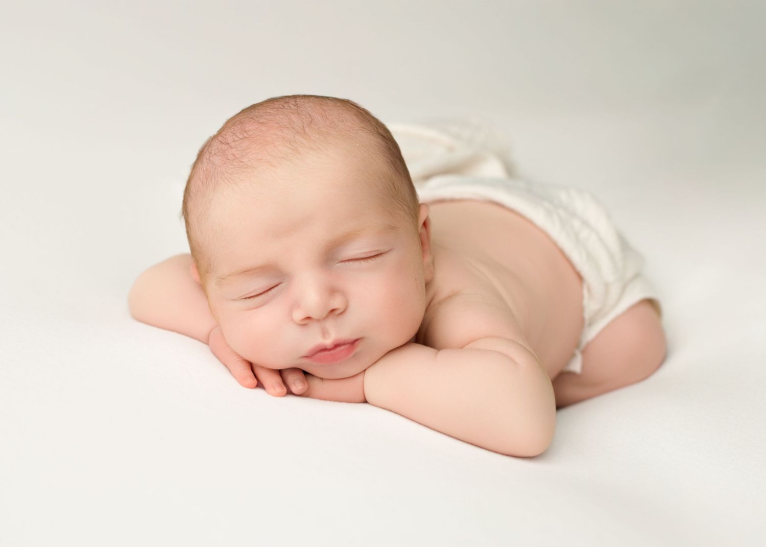 Sleeping newborn baby in white swaddle cloth laying on soft blanket in peaceful studio portrait.