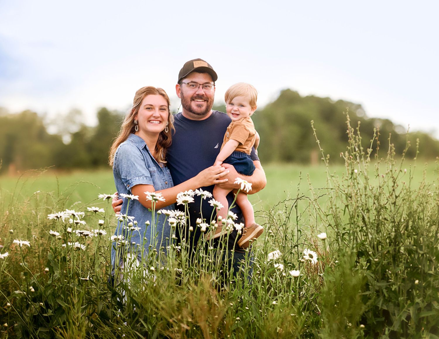A joyful outdoor family photoshoot in a sunny meadow filled with wildflowers and tall grass.