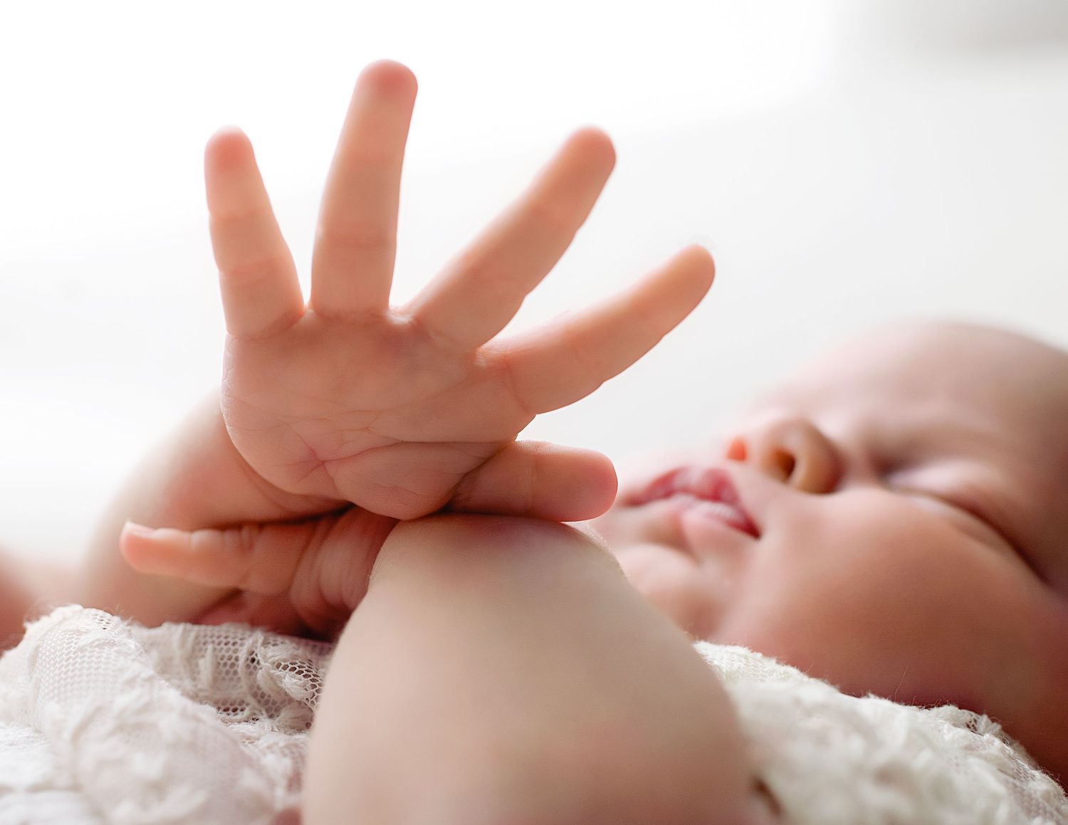 Tiny newborn hands reach upward against a soft white blanket in a series of tender moments.
