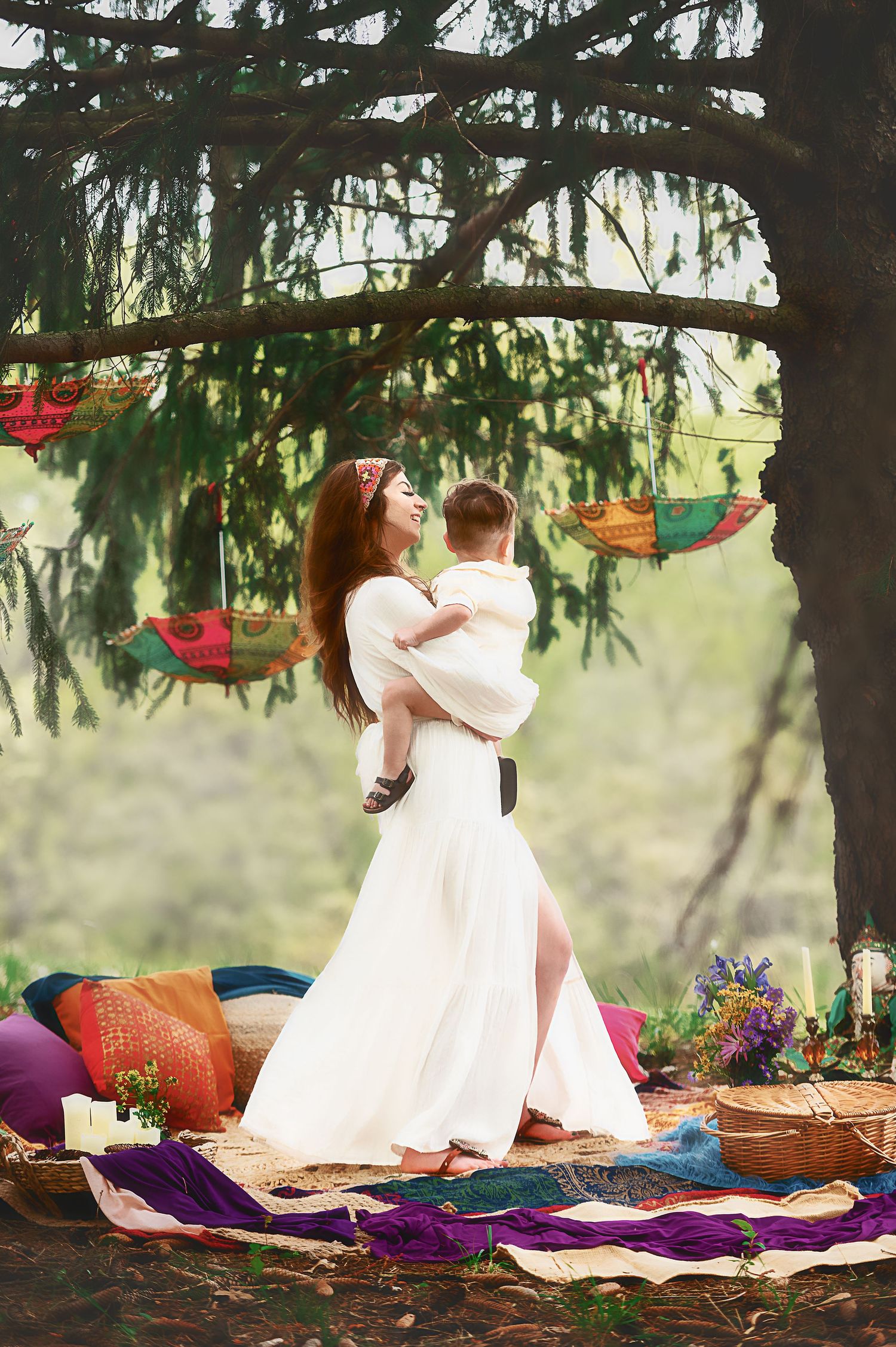 Decorative outdoor picnic setting under pine trees with colorful blankets and cushions.