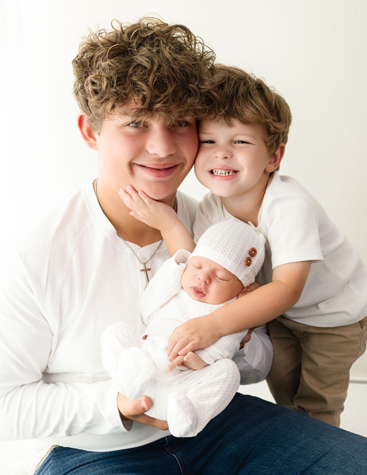 Siblings in white shirts sharing loving moments on bright studio backdrop.