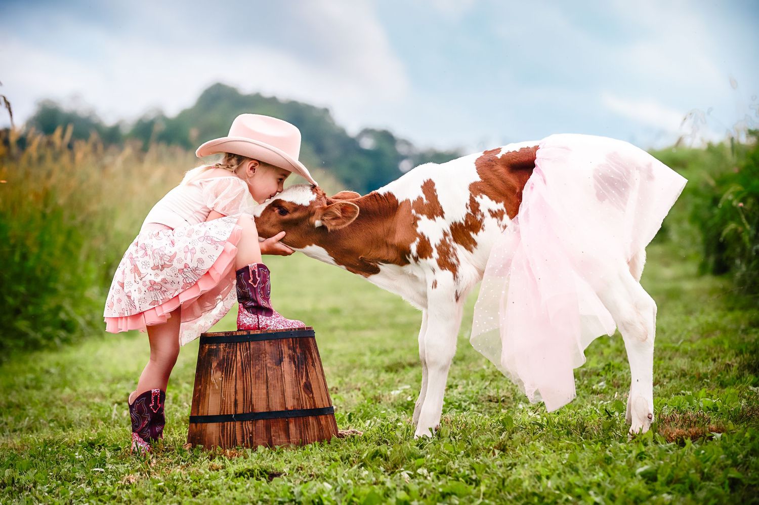 A white pony gently interacts with a child in a pink dress in a grassy meadow.