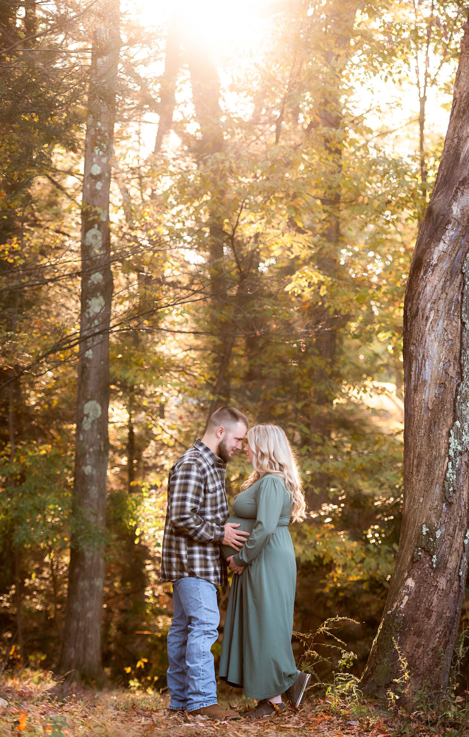 Romantic couple embraces in sunlit forest with golden autumn leaves.