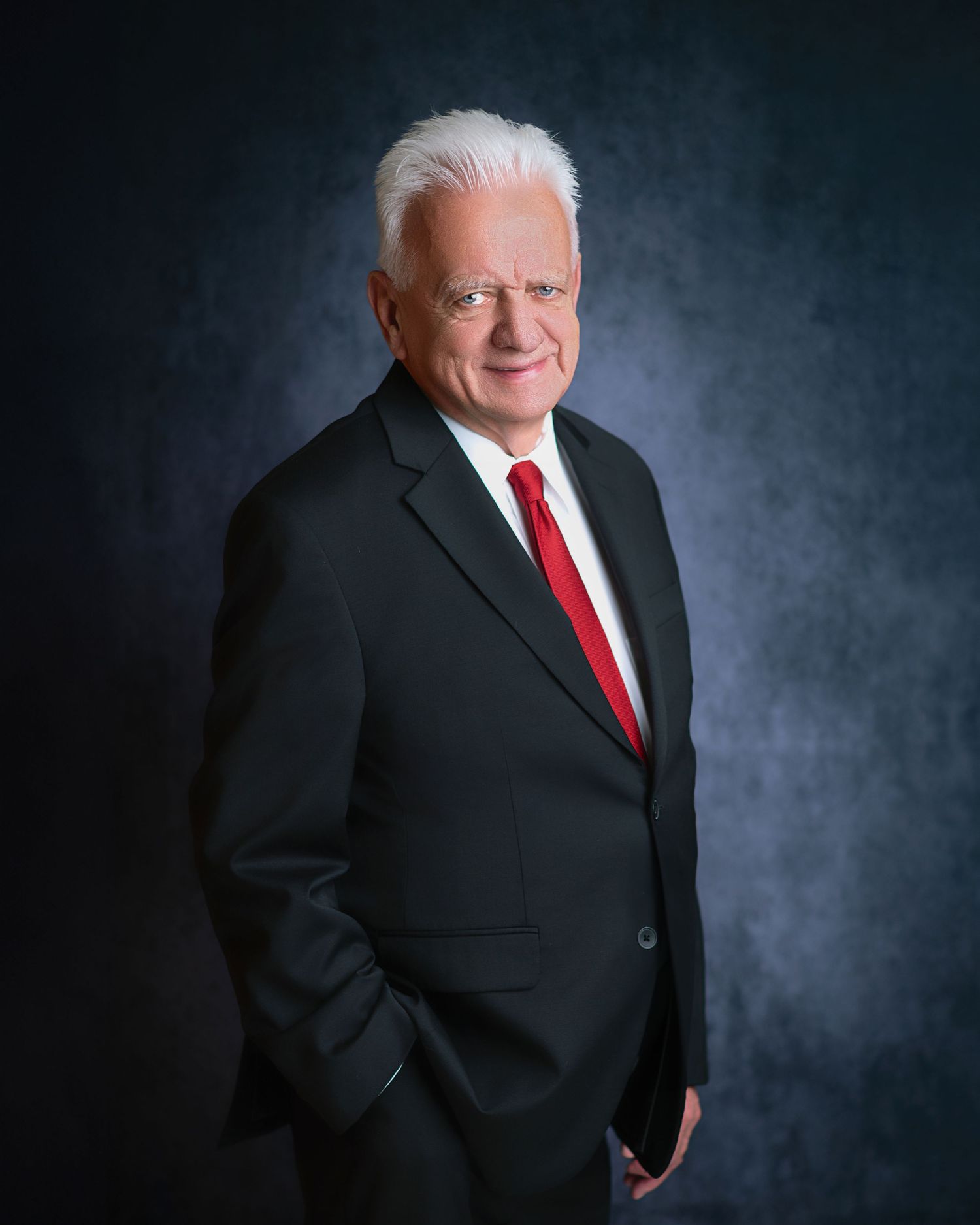 Professional headshots of man in black suit and red tie against dark background.