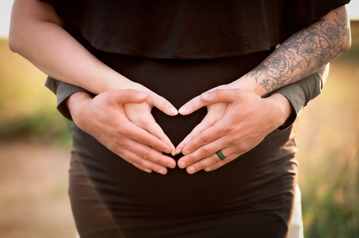 Silhouetted hands forming heart shapes at golden hour in a field.