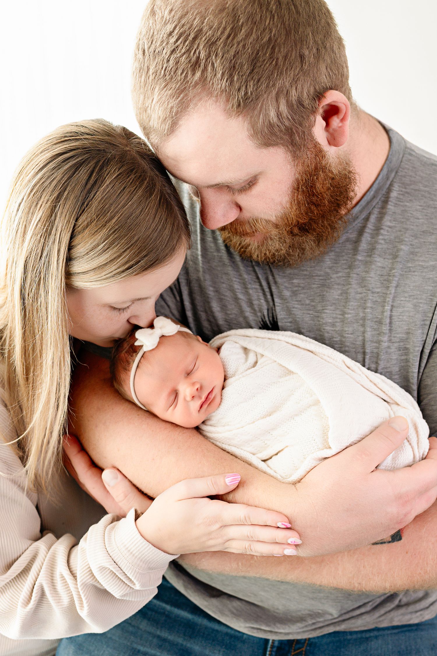 Tender family moment captured in soft light with baby wrapped in cream blanket.