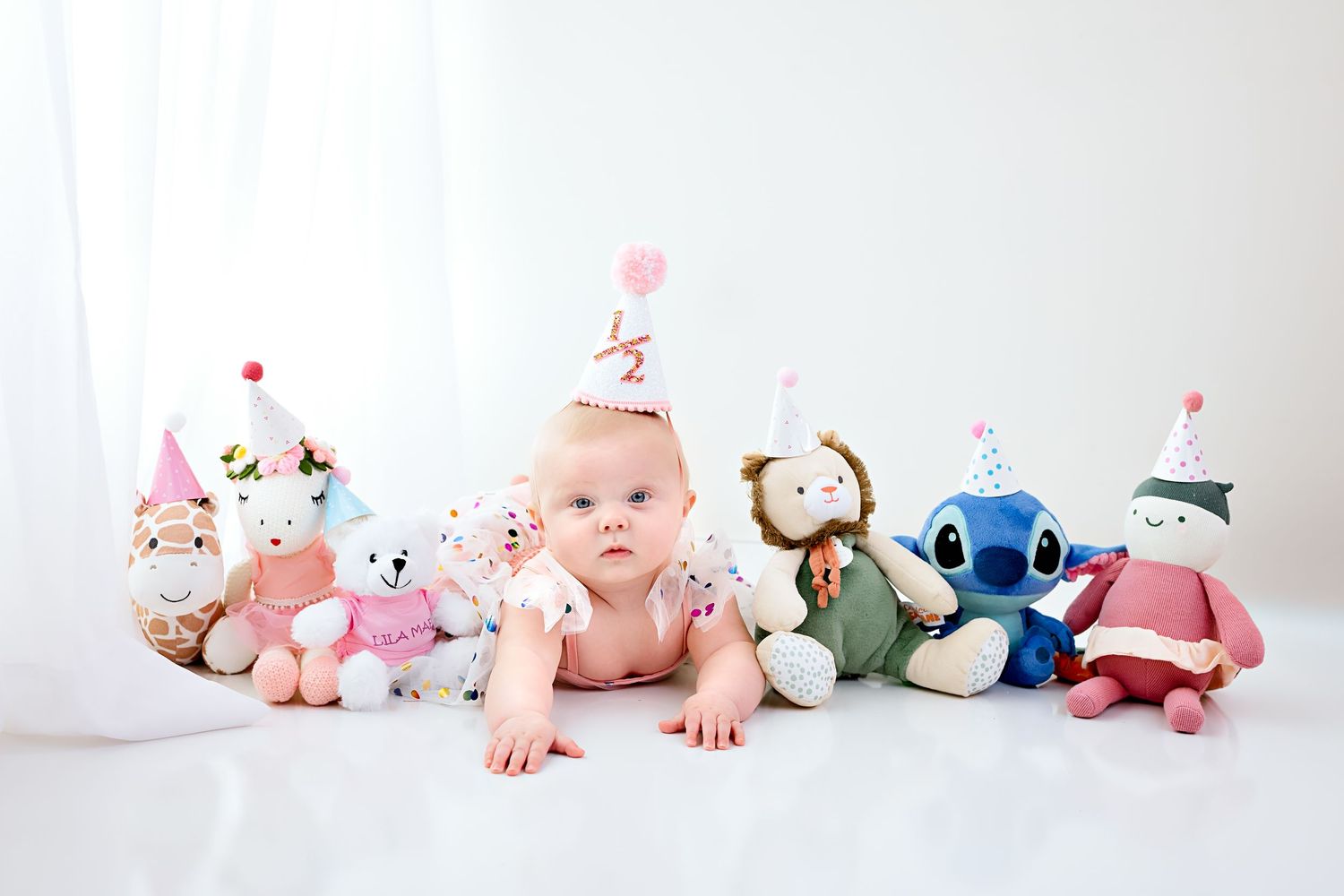 Baby photography with stuffed animal toys arranged on white background.
