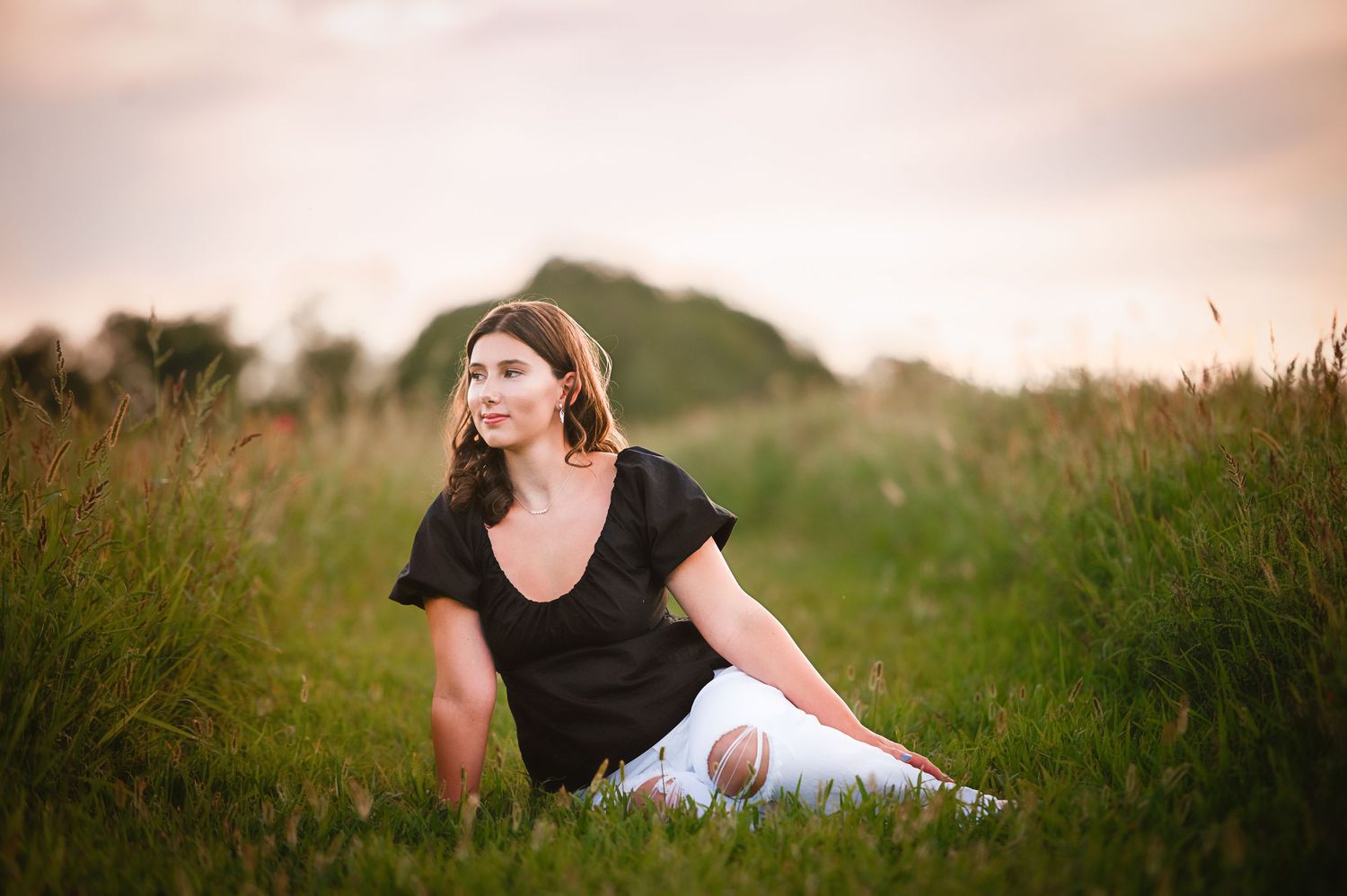 Casual outdoor portrait in black attire sitting among tall grass at dusk.