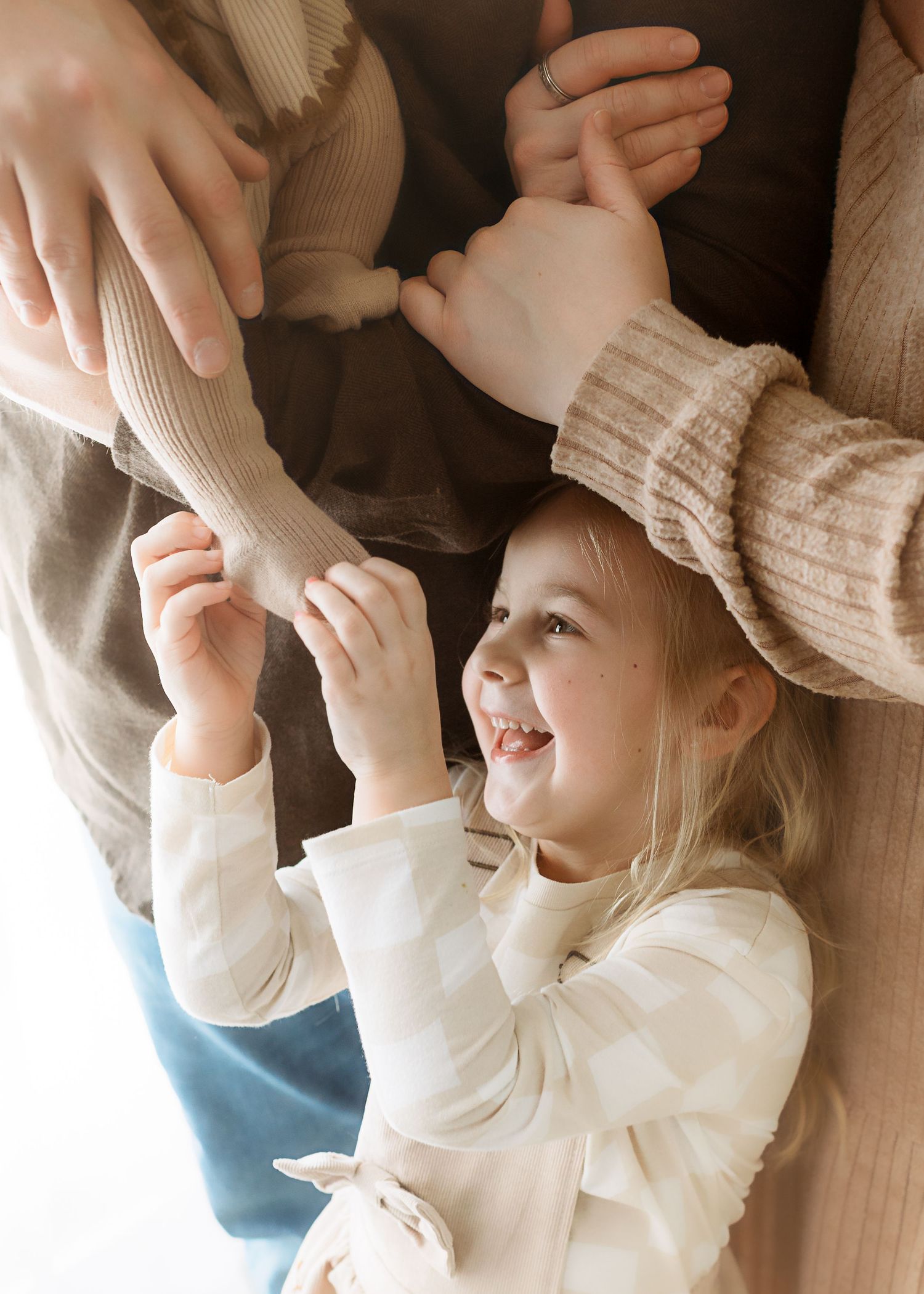 A baby in a cream sweater smiles and reaches upward while playing with someone off camera.