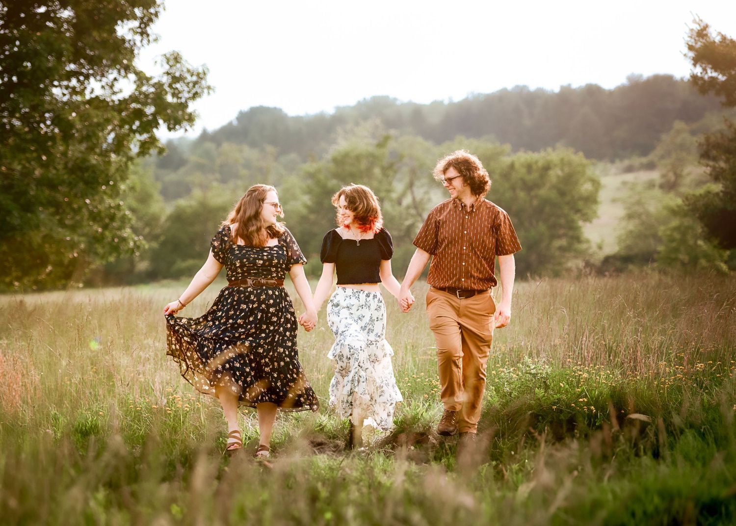 A candid family moment captured in a rustic field with rolling hills in the background.