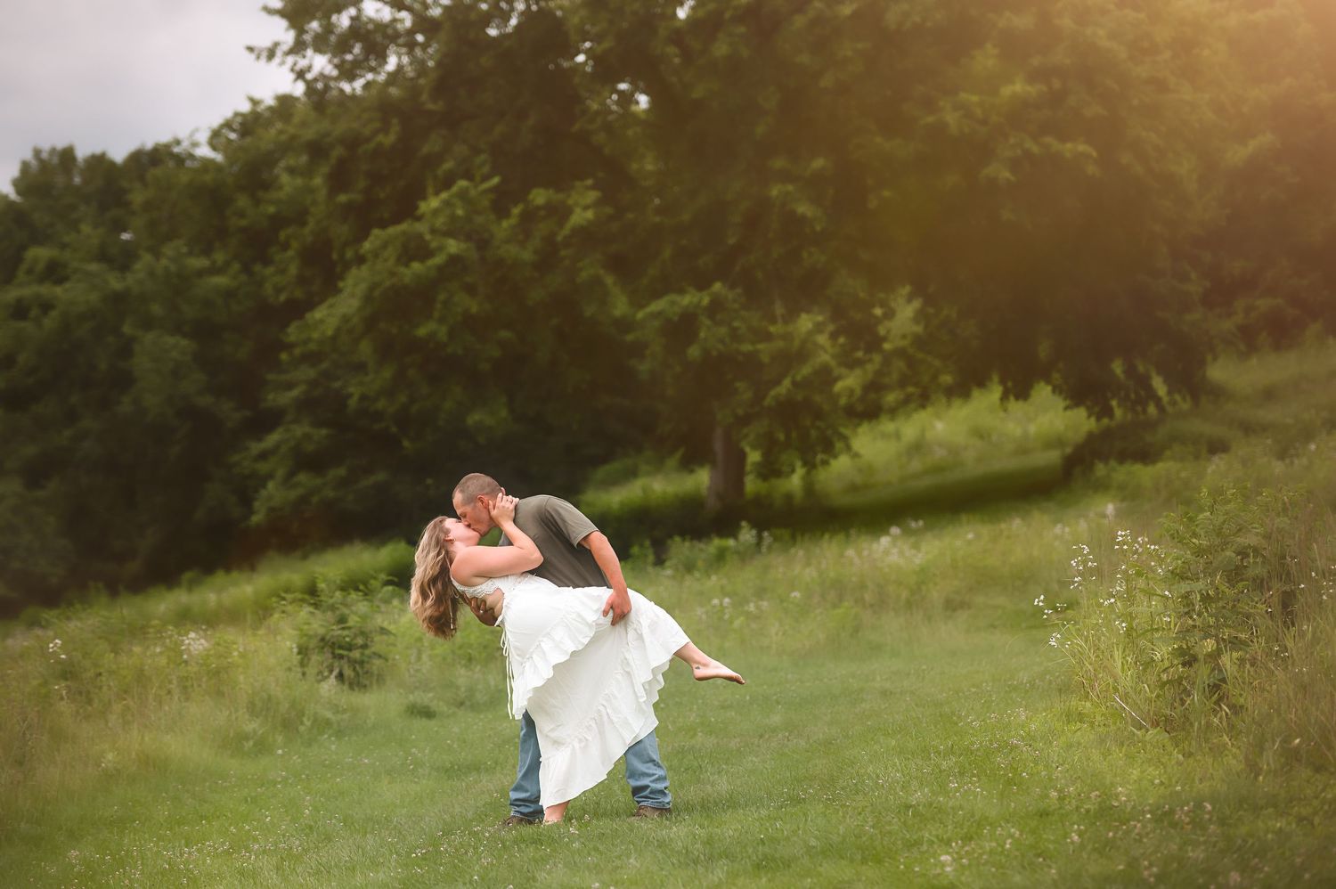 Romantic couple embraces in a sunlit meadow surrounded by nature.