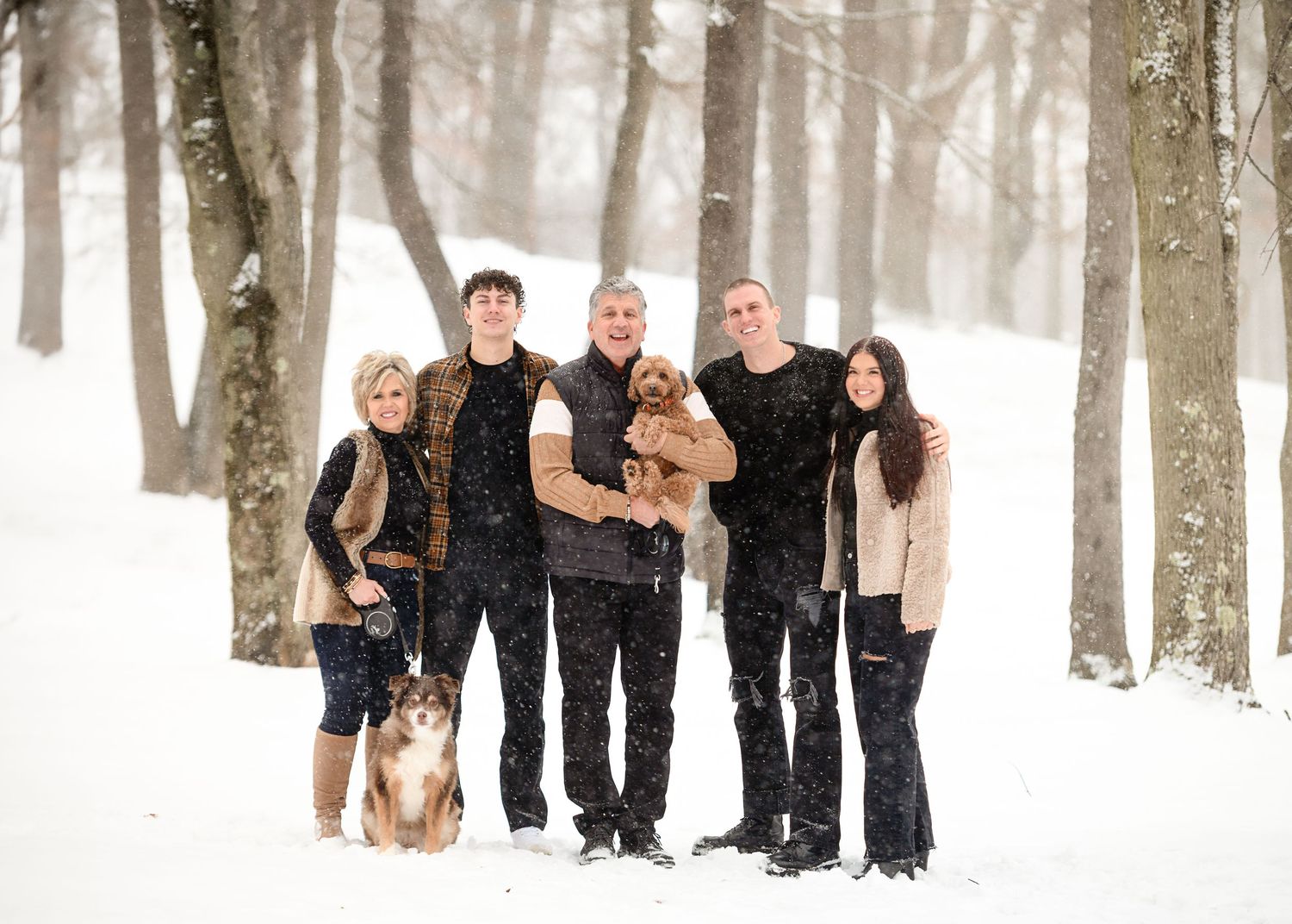 Winter family portrait in snowy forest with dog and coordinated dark outfits.