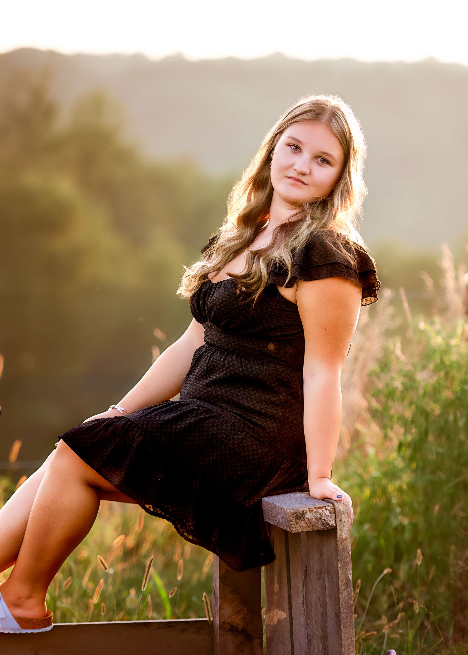 Black dress portrait session on rustic wooden bench at sunset.