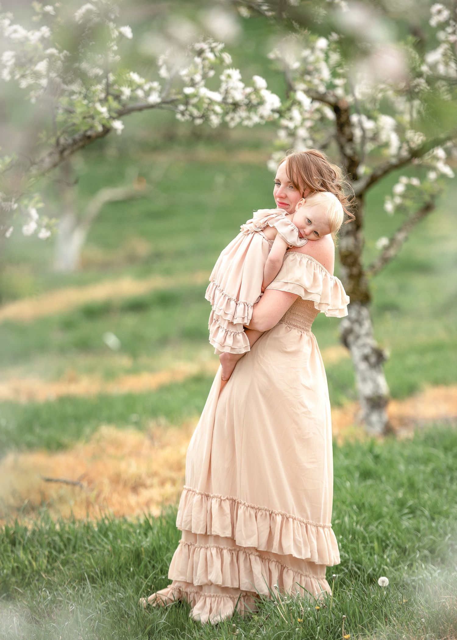 A beige ruffled dress flows gracefully in a spring orchard setting with blooming white flowers.