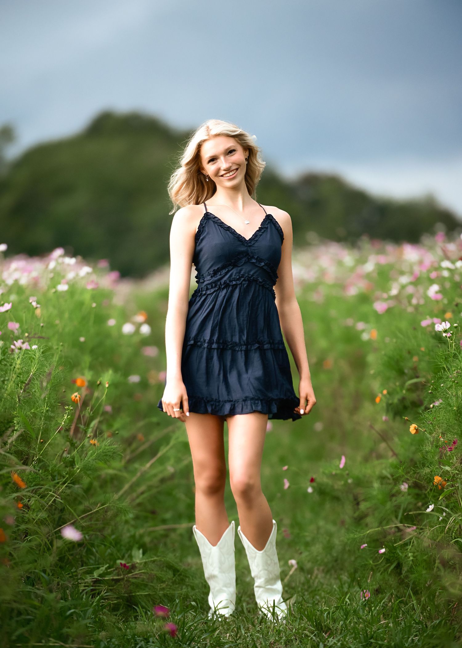 Navy blue dress and white boots contrast with wildflower meadow setting.