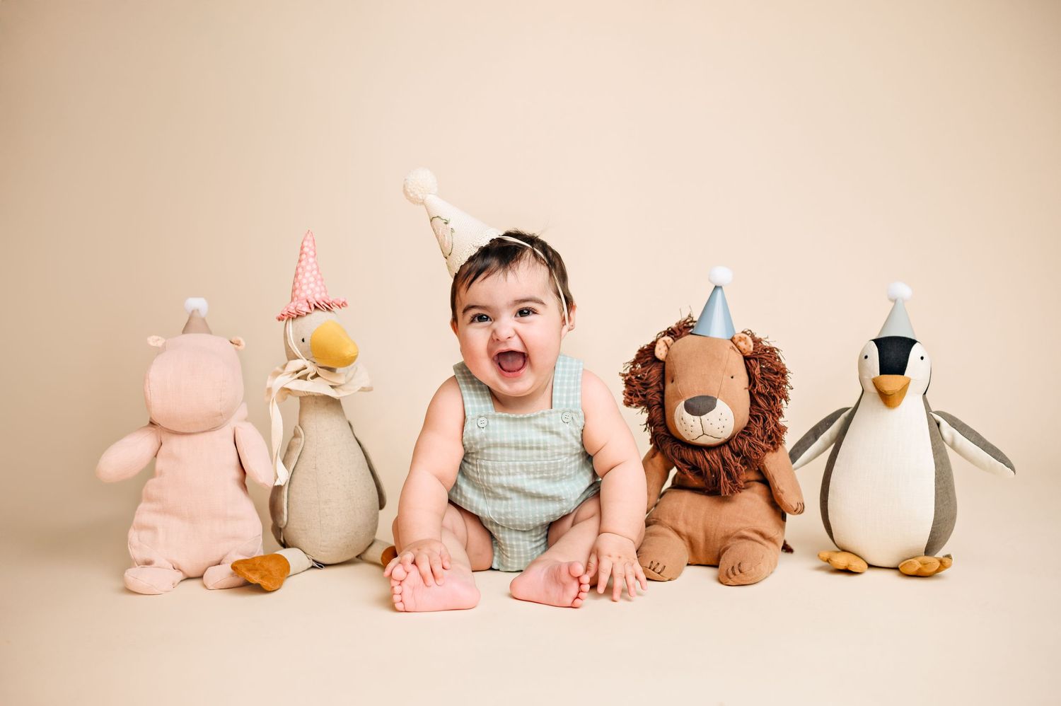 Baby milestone photo with stuffed animal collection arranged in a row on neutral background.