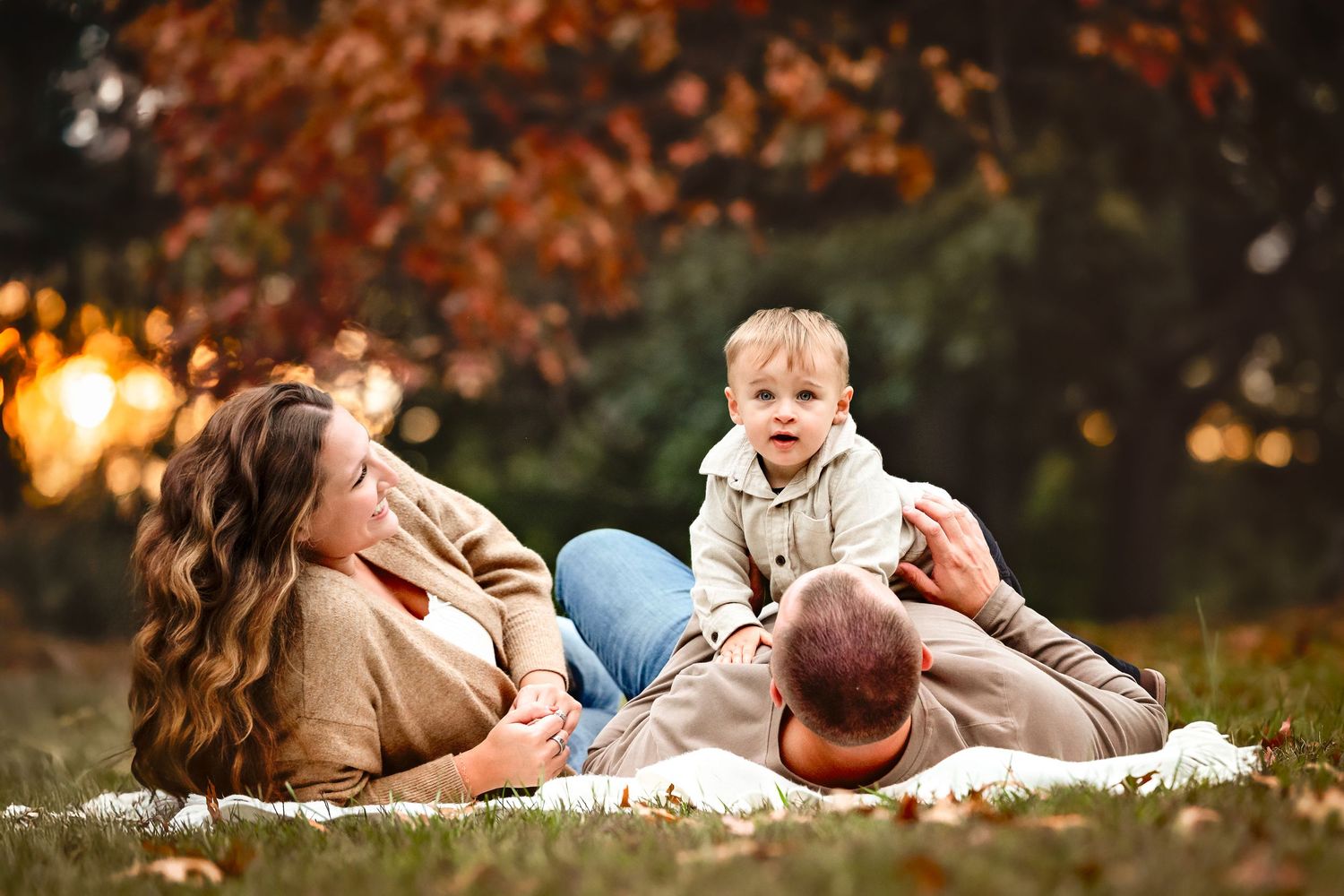 Couple lying in autumn leaves with their baby during outdoor family photo session.