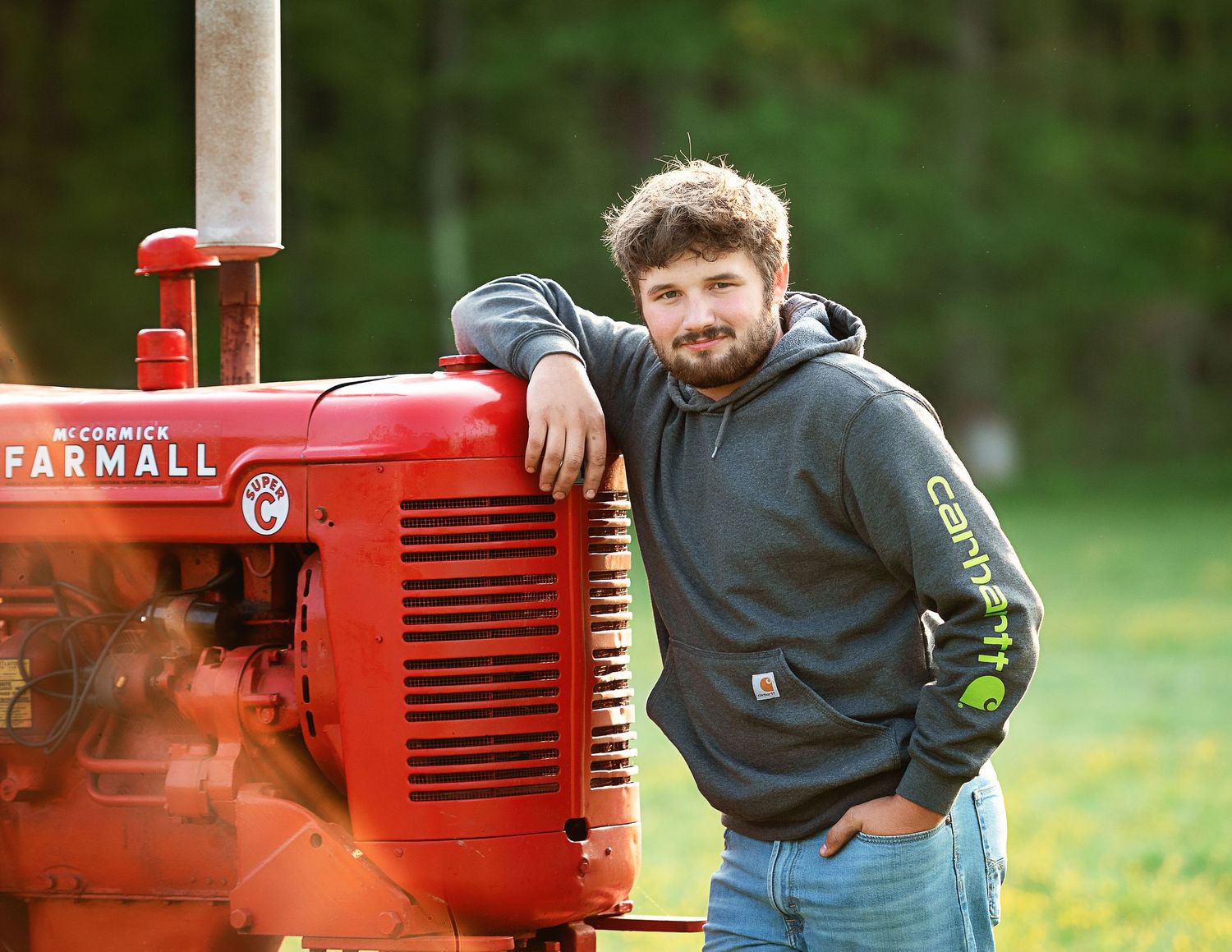 Person in hoodie poses with vintage red Farmall tractor in grassy field.