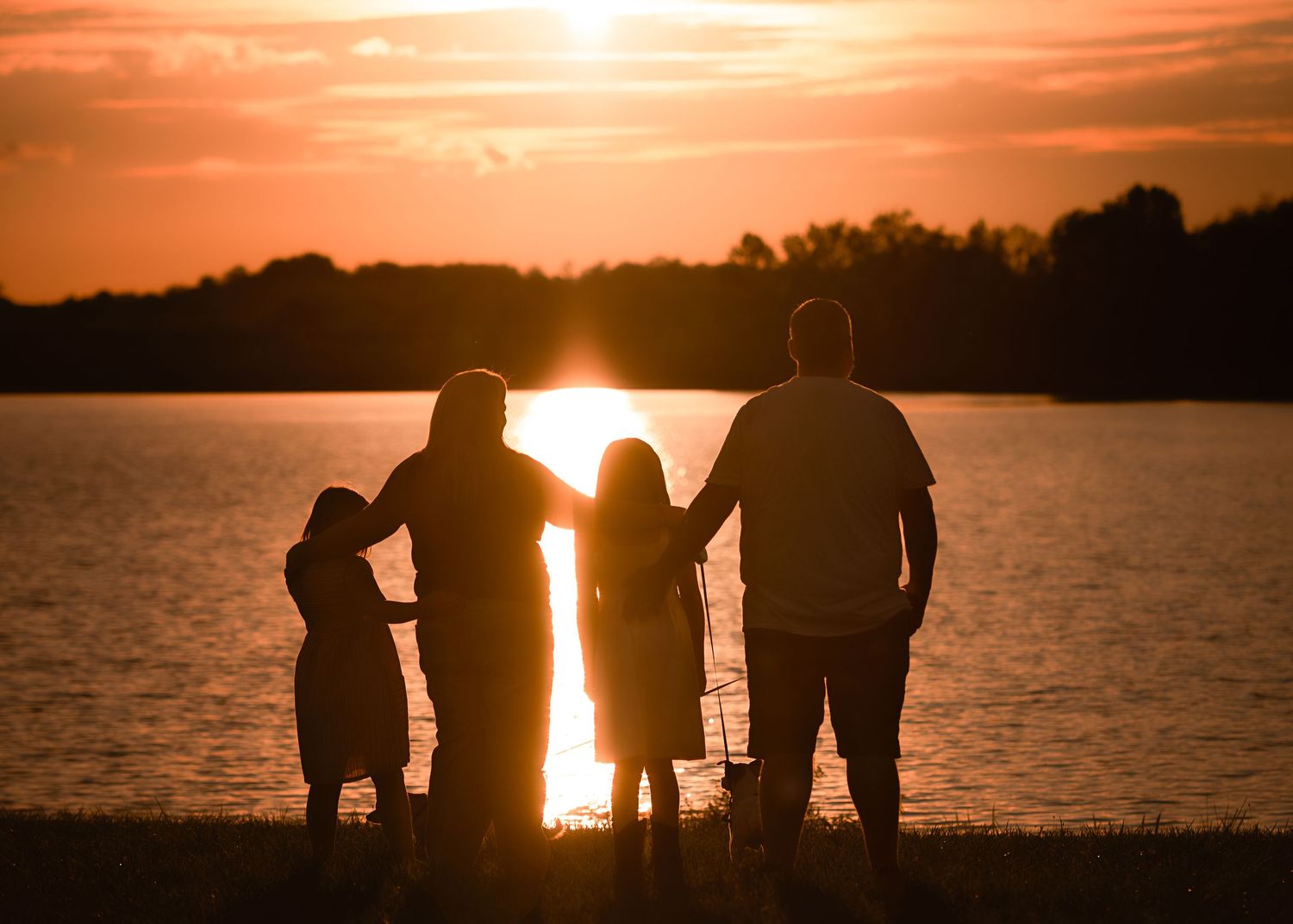 Silhouettes of a group standing by a lake during a dramatic orange sunset.