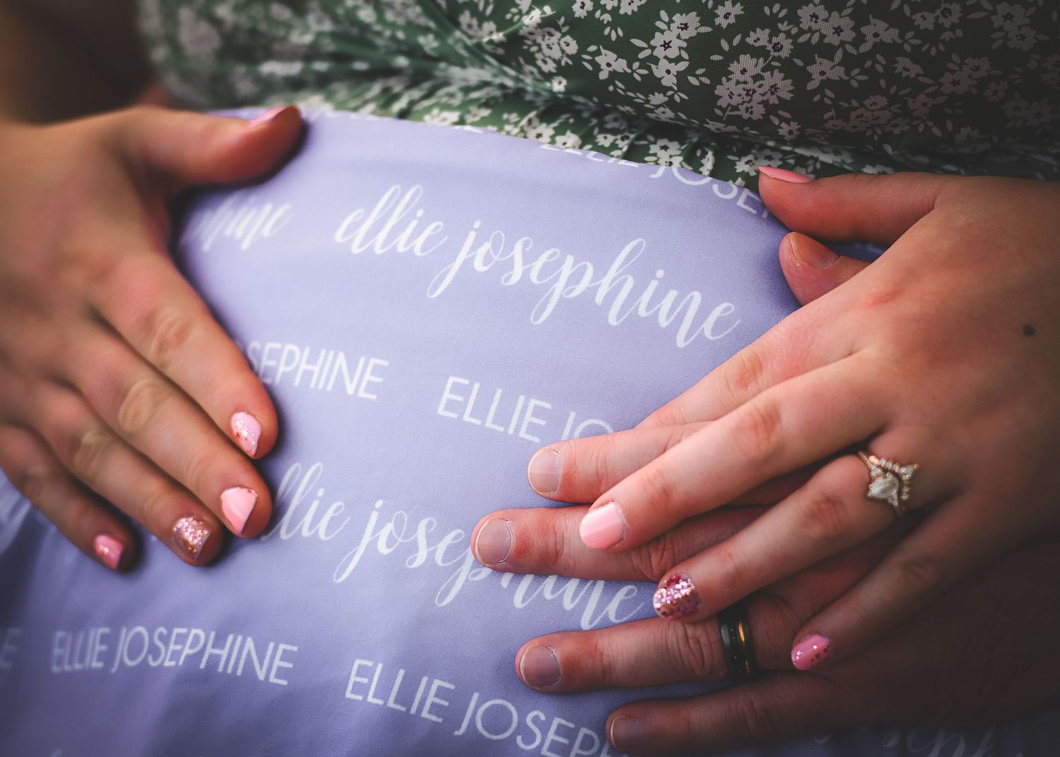 Manicured hands with red nail polish hold a purple fabric with repeating text pattern and an engagement ring.